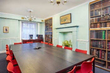 william buckland meeting room with shelves filled with books, a fireplace and a long rectangular table with red chairs around it